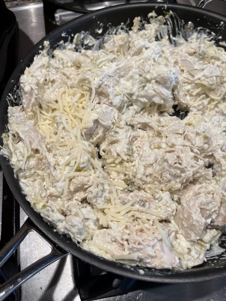 Image of skillet with shredded chicken and shredded cheese mixed in to the cream cheese and chili mixture