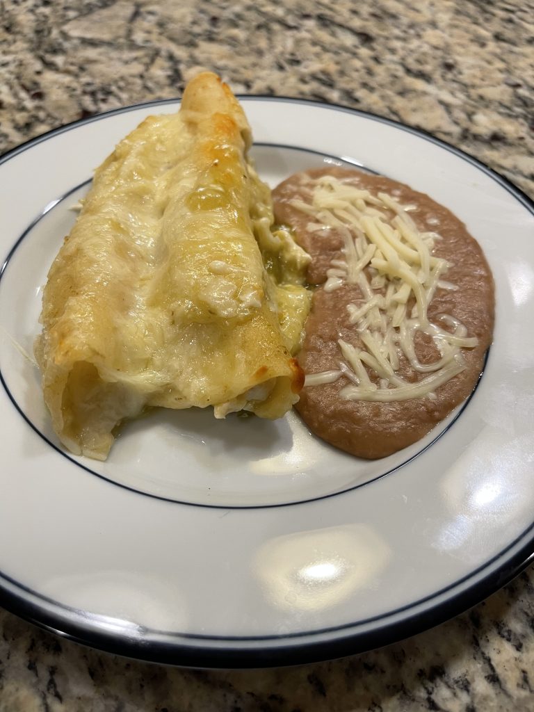 Plated Green Chili Enchiladas with a side of refried beans, topped with shredded cheese
