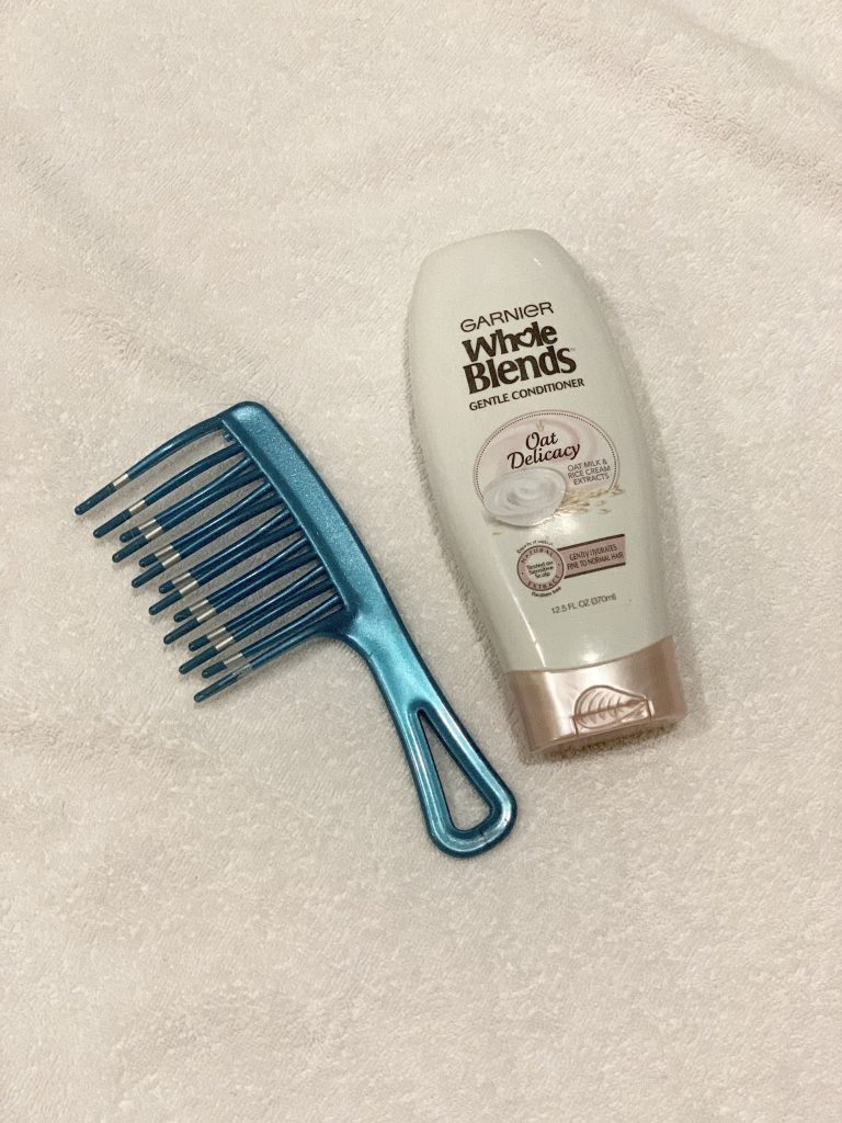 picture shows a bottle of Garnier Whole Blends conditioner and a teal wide tooth comb on a white towel