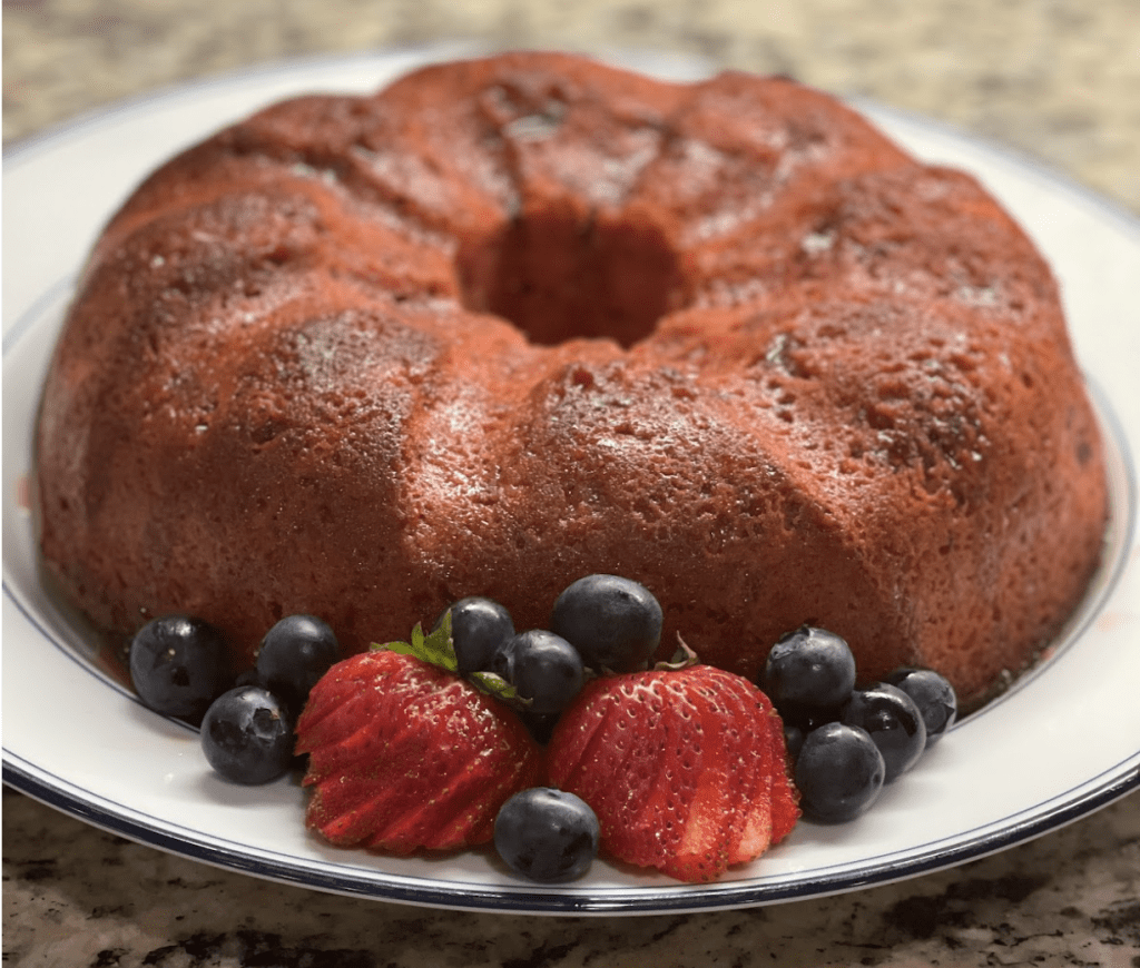 Closeup image of a freshly baked strawberry bundt cake, on a white platter, with fresh stawberries and blueberries.