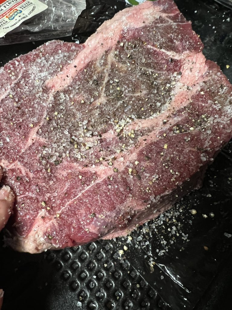 Image of an uncooked roast, seasoned with coarse kosher salt and coarse black pepper.