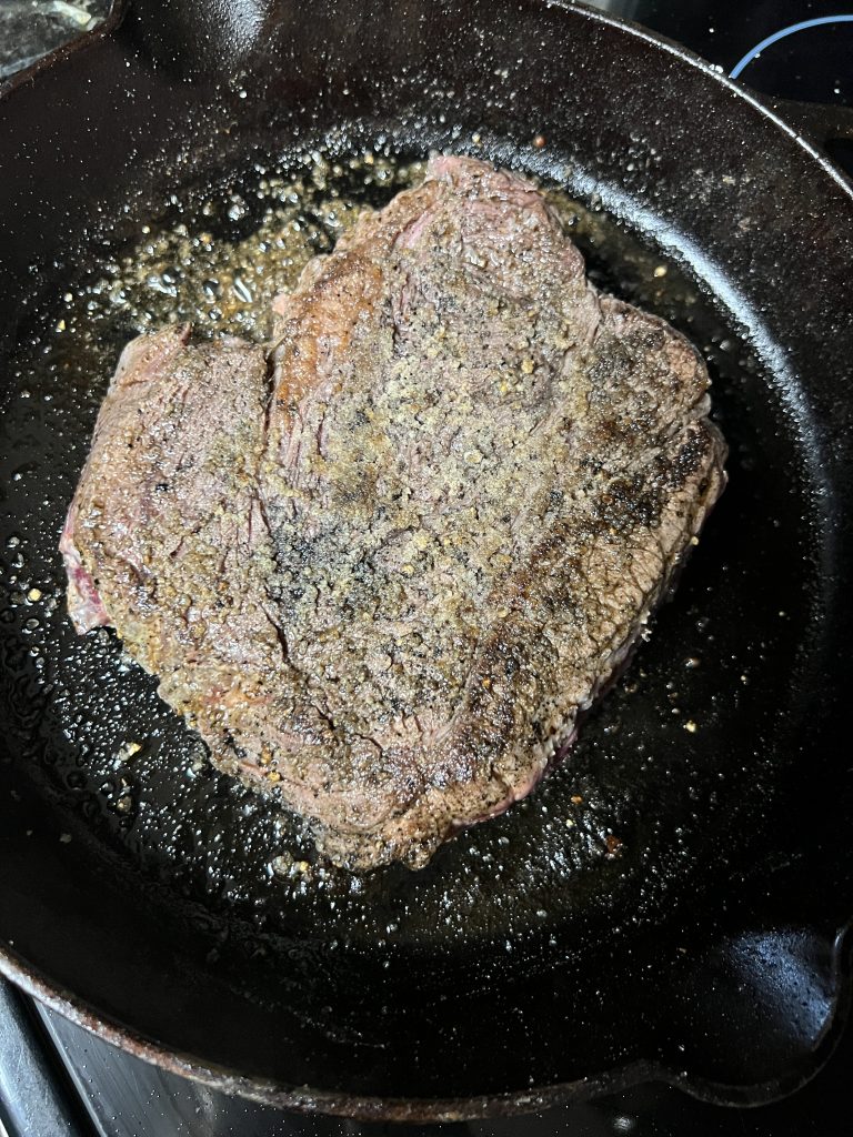 Image of a seasoned pot roast being seared in a hot cast iron skillet.