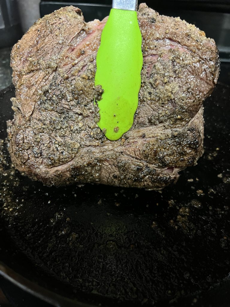 Image of seared pot roast being held with lime green tongs.
