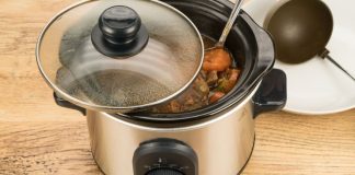 Silver crock pot, pot roast inside. There is a black ladle in the upper right corner,