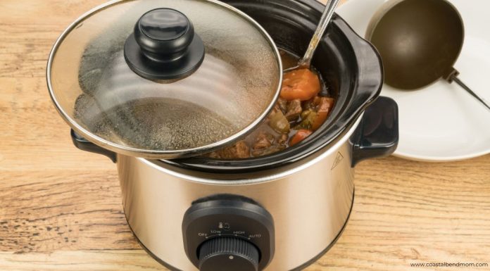 Silver crock pot, pot roast inside. There is a black ladle in the upper right corner,