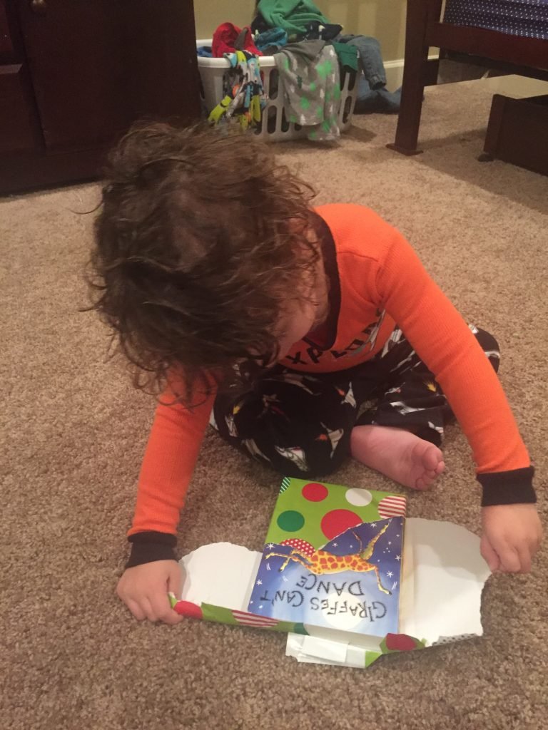2 year old boy opening a christmas gift - inside the wrapping paper is a book