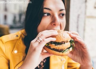 Woman in a yellow jacket eating a hamburger