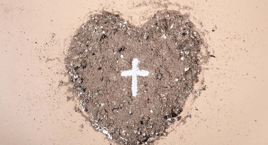 A heart made out of sand with the images of a white cross in the center of the heart.