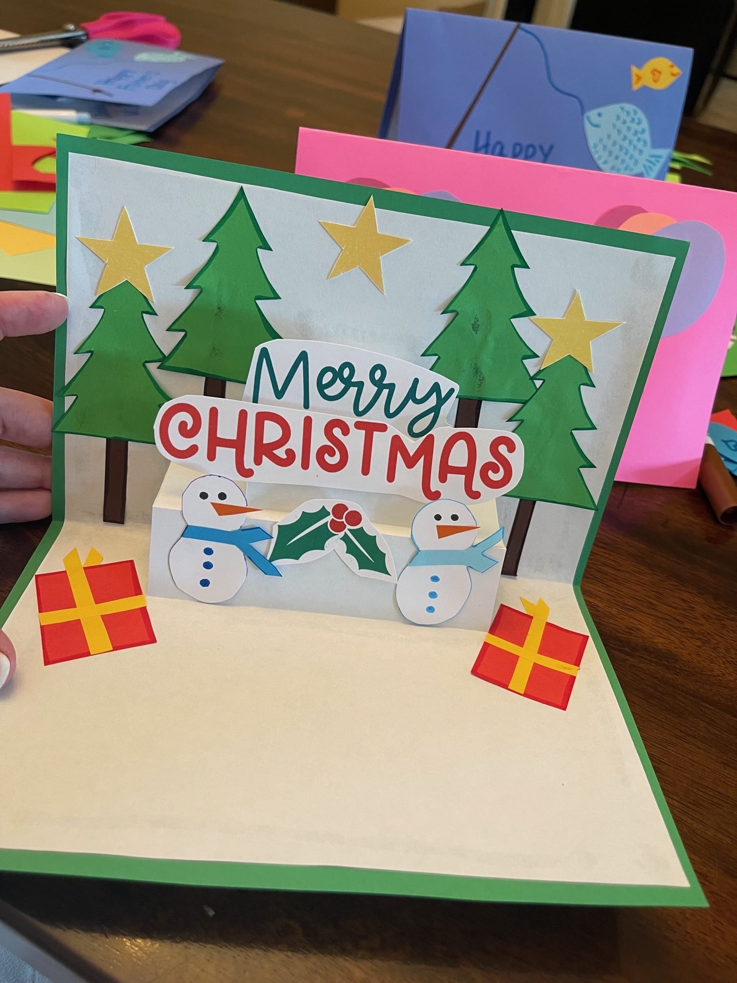 finished product of a Christmas card with trees, snowmen, presents and Merry Christmas banner