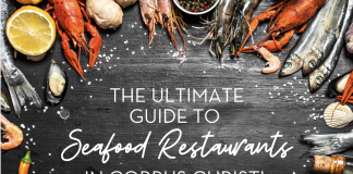 Black slate background, with an assortment of fresh seafood items creating a border. The text in the center reads "The Ultimate Guide to Seafood Restaurants in Corpus Christi"